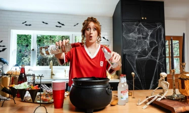 Brittany Broski pouring Smirnoff Ice into a cauldron with Halloween decorations surrounding it.