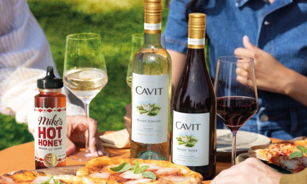 Cavit Pinot Noir and Pinot Grigio with Mike's Hot Honey on a table with pizza and people dining.