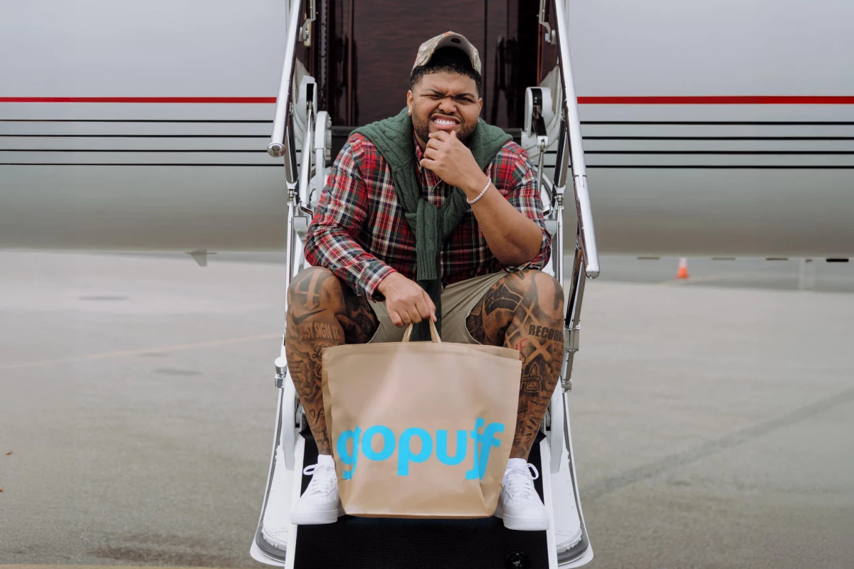 Druski sitting on the staircase of an airplane with a gopuff handbag