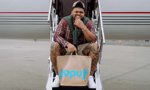 Druski sitting on the staircase of an airplane with a gopuff handbag