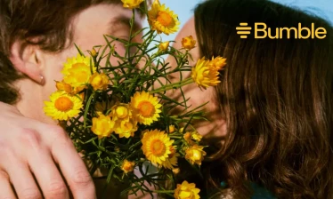 A man and a woman kissing with sunflowers covering the kiss, the Bumble logo on the upper right