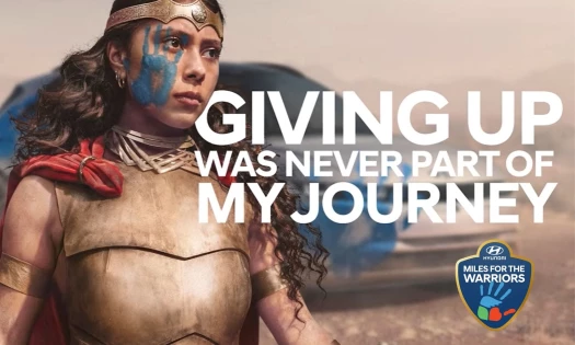 Young girl in a warrior outfit with the Hyundai Hope on Wheels painted handprint on her face.