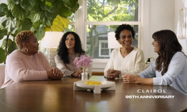 Four women sit around a table with the Clairol logo and 95th Anniversary in the bottom left corner.
