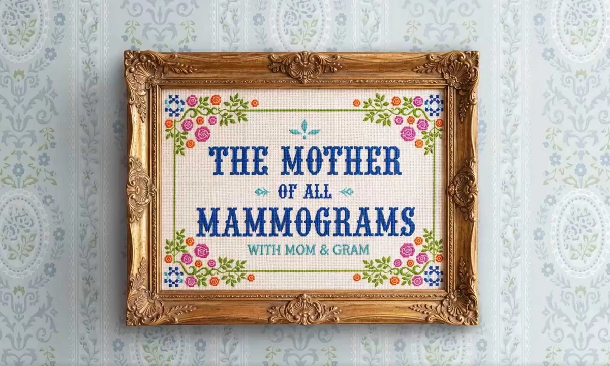 A needlepoint artwork of "The Mother of All Mammograms with Mom & Gram" framed and hung against a wall.