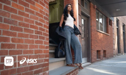 A woman standing at the foot of the steps of a brick-faced building, wearing a pair of ASICS.