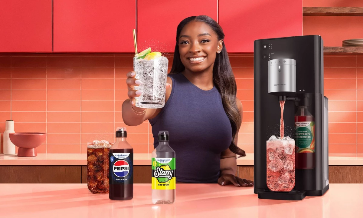 Simone Biles behind a kitchen counter with the SodaStream Fountain, and the Pepsi and Starry syrups.