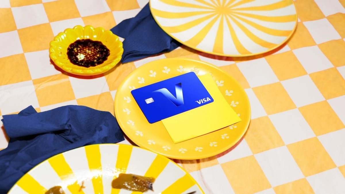 A VISA credit card with the V logo on a yellow plate on a yellow checkered lunch table