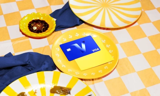 A VISA credit card with the V logo on a yellow plate on a yellow checkered lunch table
