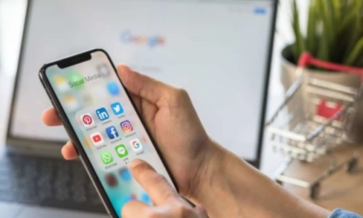 A man looking at phone and laptop to decide between Facebook and Google