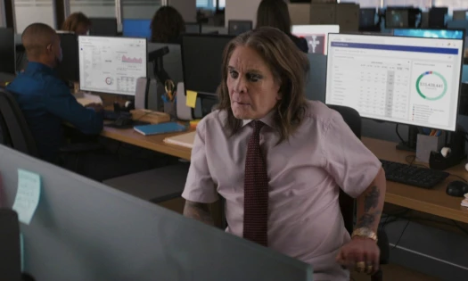Ozzy Osbourne in formal shirt and tie with black eyeliner sitting in an office cubicle