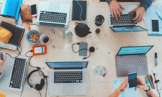 People crowded around a communal working table with laptops and other gadgets