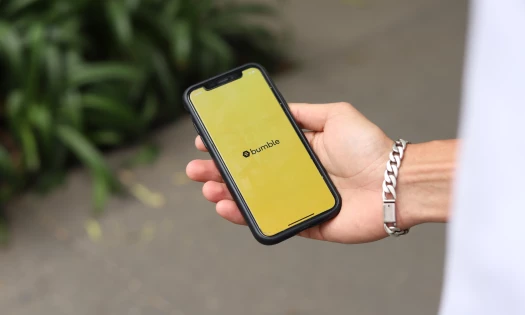 Hand holding a smartphone with the Bumble dating app application logo on the screen