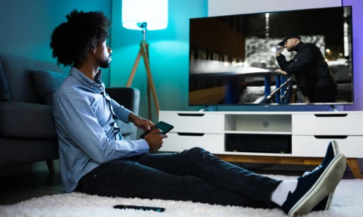 Photograph of a man sitting o the floor of his living room, watching a movie on a big screen