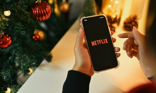 Festive image of a person holding a smartphone with the Netflix app and logo on the screen