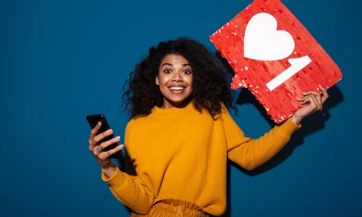 Stock image of a happy woman holding a smartphone in her one hand, and a 'heart like' sign in the other