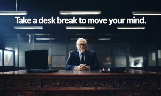 Brian Cox sits behind an office desk