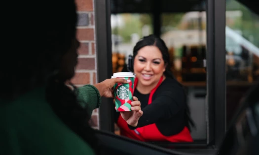 A woman hands a customer their Starbucks drink