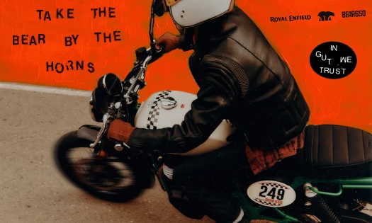 A rider on the Royal Enfield Bear 650 with 'In Gut We Trust' graphics