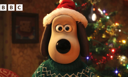 Gromit wearing a Santa hat and Christmas sweater standing in front of a Christmas tree