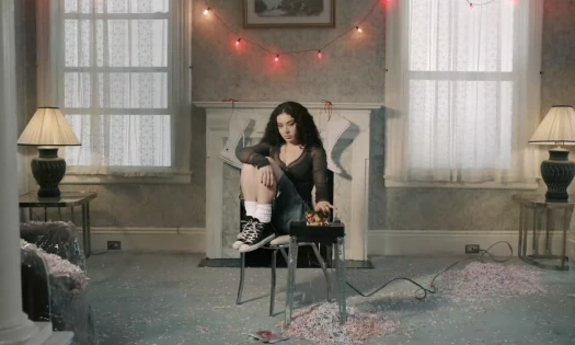 Charli XCX in a cozy living room, shredding Christmas postcards.