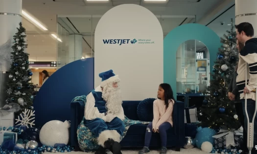 Santa Claus and a child at the airport with a WestJet themed background.