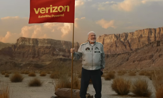 Dr. Buzz Aldrin holding a red Verizon flag at a desert