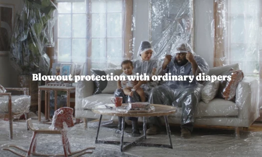 A living room covered in plastic with parents wearing the Poop Poncho for "blowout protection"