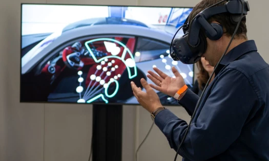 A man with a VR headset on, looking at his hands with a screen in the background displaying what he sees