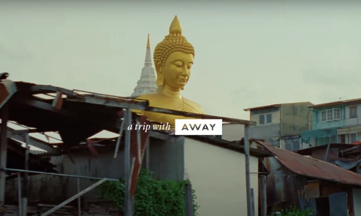 A gold statue in Thailand with text: "a trip with AWAY"