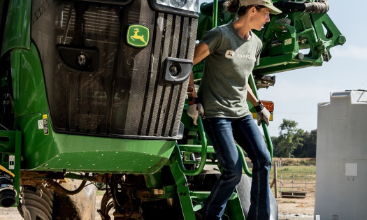 A woman getting off a green tractor wearing the new workwear collection for female farmers
