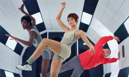 Zendaya posing in a spaceship wearing On workout clothes and shoes, with two of her astronaut crew members