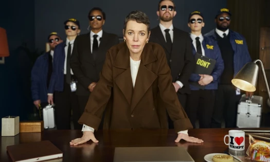 Olivia Coleman leaning on a table with inspectors behind her