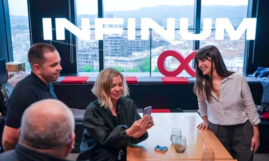 A group of people gathered around a table, looking at a cellphone in a woman's hand. Infinum's logo in the window.