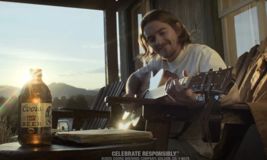 A man playing the guitar with a Coors Banquet bottle in the foreground