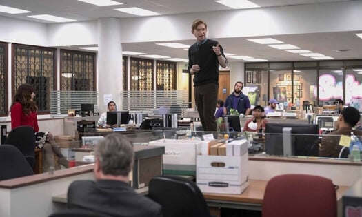 Domhnall Gleeson standing on a desk while the rest of the cast of "The Paper" look on