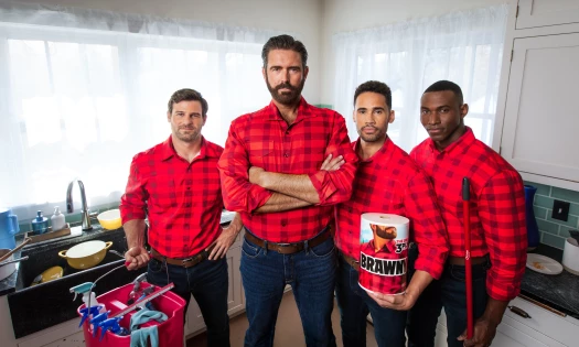 The Brawny Man with the "3-Ply Guys" in the kitchen wearing matching red, plaid shirts holding the the 3-ply paper towel and cleaning tools