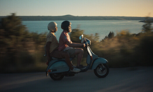 Two guys on a moped driving on a road by the beach