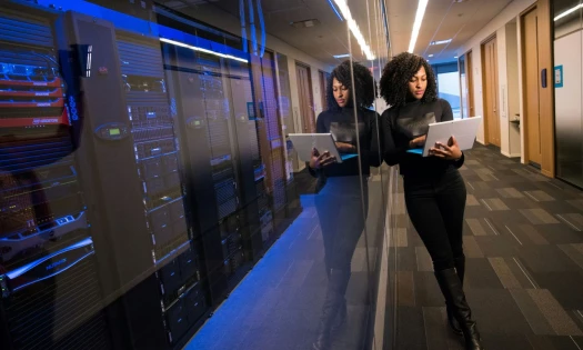 A woman holding a laptop next to a server rack