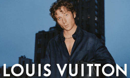 Jeremy Allen White poses with a cityscape backdrop and "Louis Vuitton" printed in white