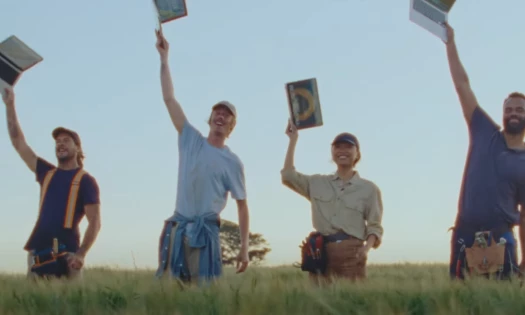 Four people in a grassland raise their laptops into the air