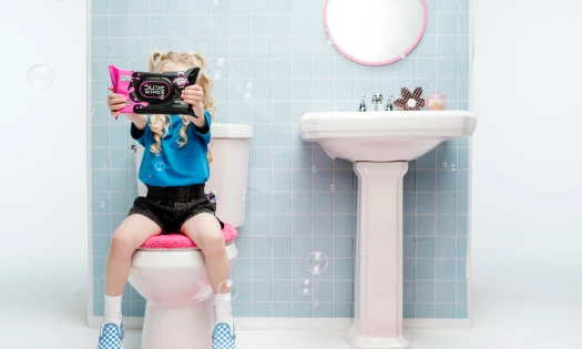 A little lady sitting on a toilet holding up the new 'LiL DUDE Wipes'
