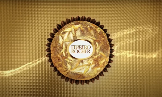 A Ferrero Rocher chocolate in gold background with gold swirls