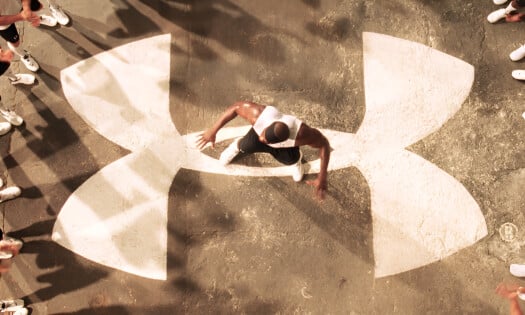 Eric "Big E" Ogbogu standing at the center of a big Under Armour logo with athletes clapping surrounding him from the brand's first national TV ad, "Protect this House"