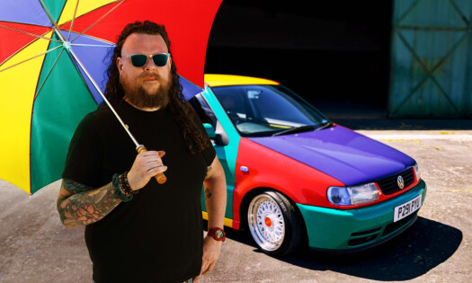 A man carrying a colorful umbrella beside his Volkswagen vehicle