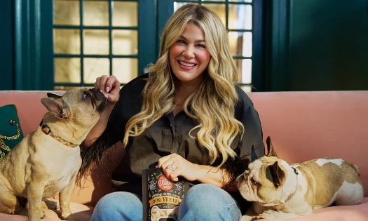 Heather McMahan sits on a couch with two dogs by her side