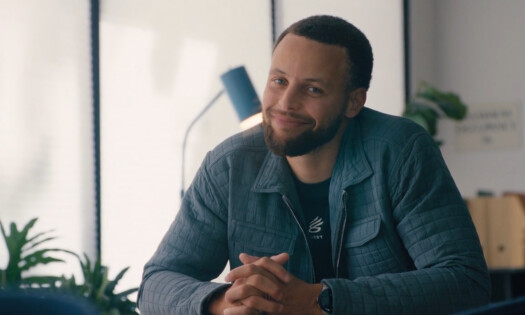 Stephen Curry behind the desk smiling at the camera