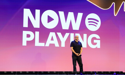 Spotify Founder Daniel Ek standing on stage with a pink screen behind him with the text: NOW PLAYING