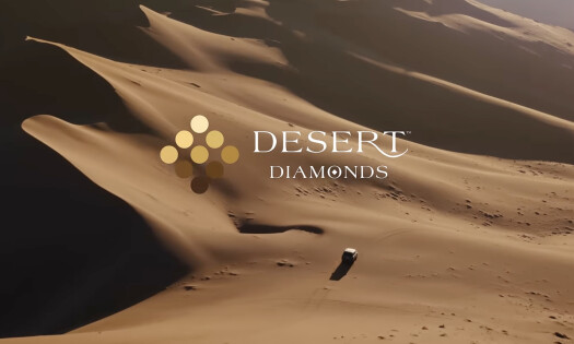 The De Beers logo with the text "Desert Diamonds" over a real desert landscape with a car driving below