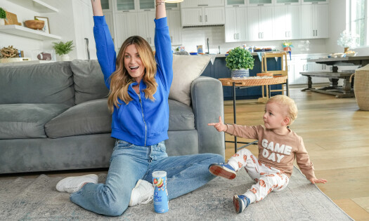 Erin Andrews with her arms raised and her baby boy in the living room watching a football game with a Gerber product
