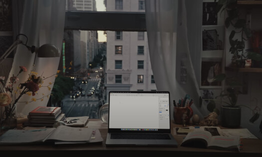 A Macbook lays open on a desk facing the city